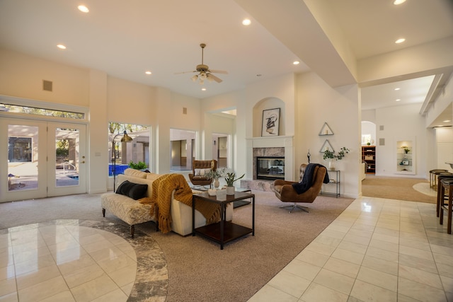 carpeted living room with ceiling fan, a towering ceiling, a fireplace, and french doors