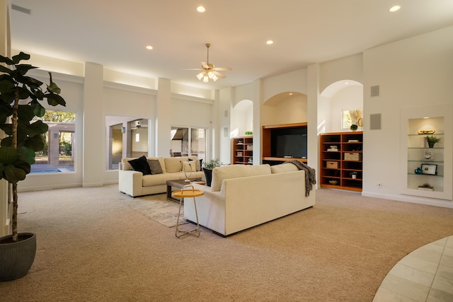 living room featuring ceiling fan, light colored carpet, built in features, and a high ceiling