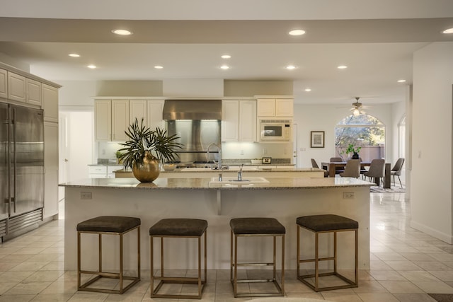 kitchen featuring ceiling fan, stone counters, a kitchen breakfast bar, built in appliances, and an island with sink