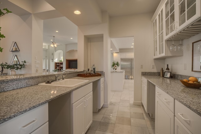 kitchen featuring stainless steel built in refrigerator, sink, white cabinetry, ceiling fan, and light stone countertops