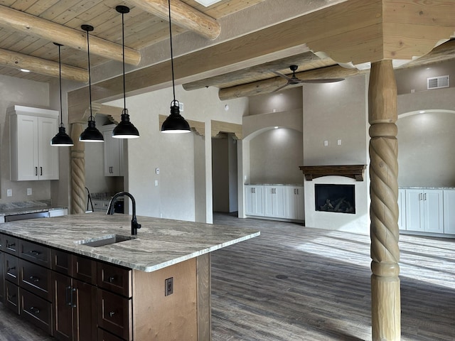 kitchen with pendant lighting, sink, white cabinetry, a kitchen island with sink, and light stone countertops