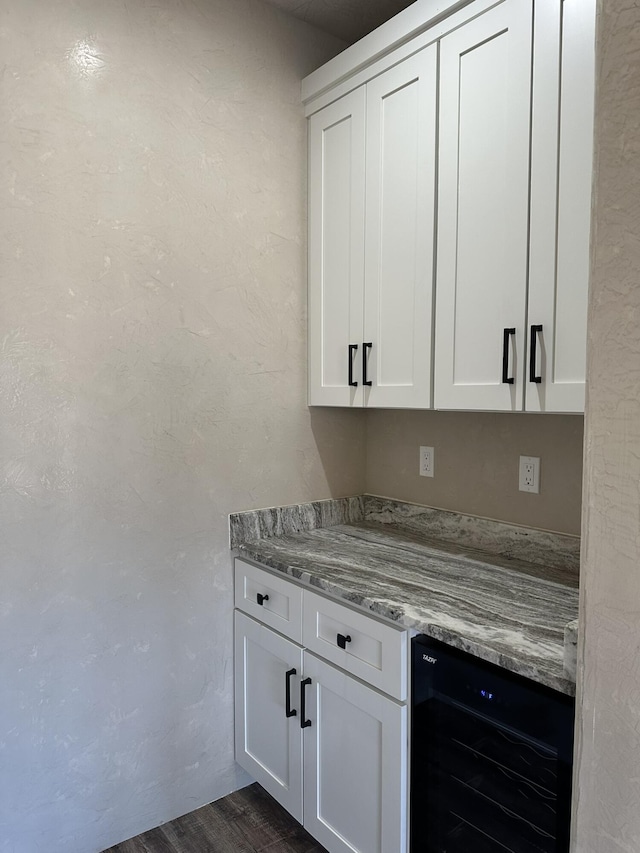 bar with wine cooler, light stone countertops, and white cabinets