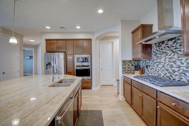 kitchen with sink, wall chimney exhaust hood, light hardwood / wood-style floors, pendant lighting, and appliances with stainless steel finishes