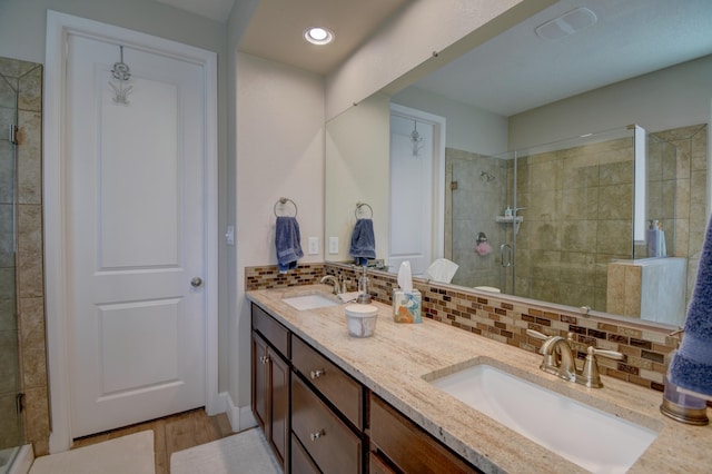 bathroom featuring hardwood / wood-style floors, vanity, a shower with shower door, and tasteful backsplash