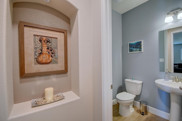 half bath with baseboards, a sink, toilet, and wood finished floors