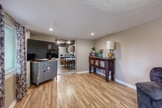 living area with a textured ceiling, recessed lighting, light wood-type flooring, and baseboards