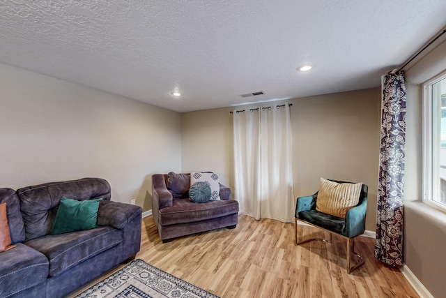 living area with plenty of natural light, a textured ceiling, light wood-type flooring, and visible vents