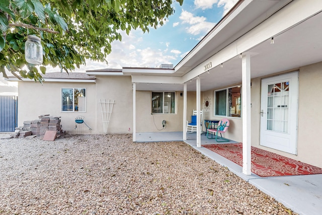 view of exterior entry featuring a patio area, fence, and stucco siding