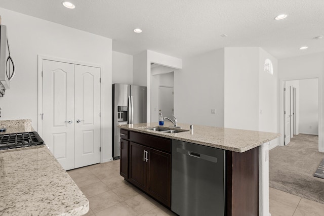 kitchen featuring dark brown cabinetry, sink, stainless steel appliances, an island with sink, and light carpet