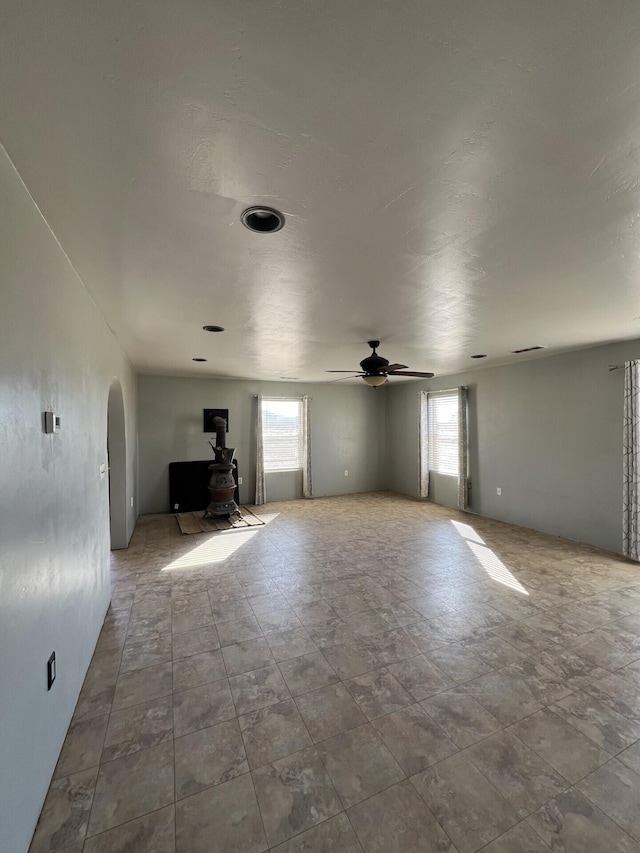 unfurnished living room with a wood stove, plenty of natural light, and ceiling fan