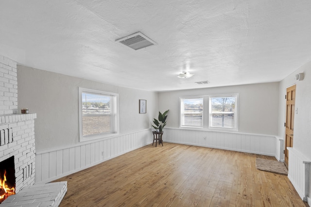 unfurnished living room featuring light wood-type flooring, a textured ceiling, and a brick fireplace