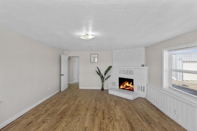 unfurnished living room featuring hardwood / wood-style flooring and a brick fireplace