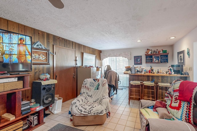 living room featuring wood walls, light tile patterned floors, a textured ceiling, and ceiling fan