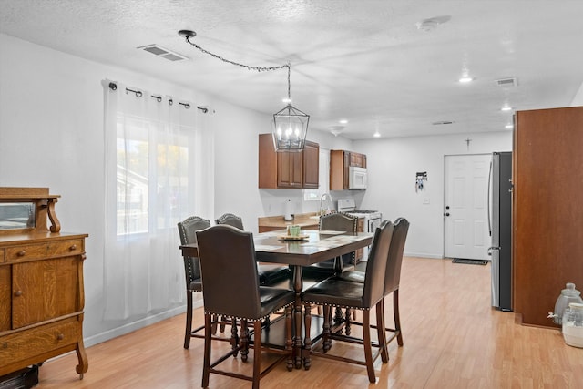 dining space with a chandelier, light hardwood / wood-style floors, and a textured ceiling