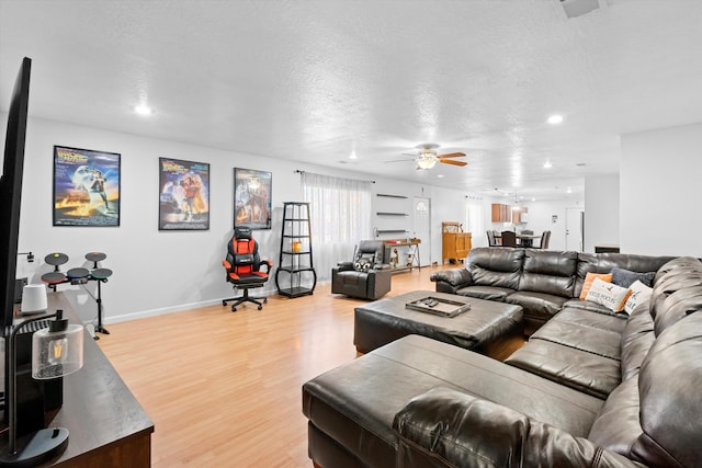 living room featuring a textured ceiling, light wood-type flooring, and ceiling fan