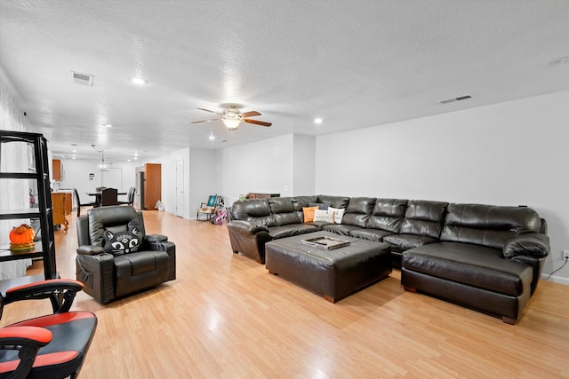 living room featuring ceiling fan, light wood-type flooring, and a textured ceiling