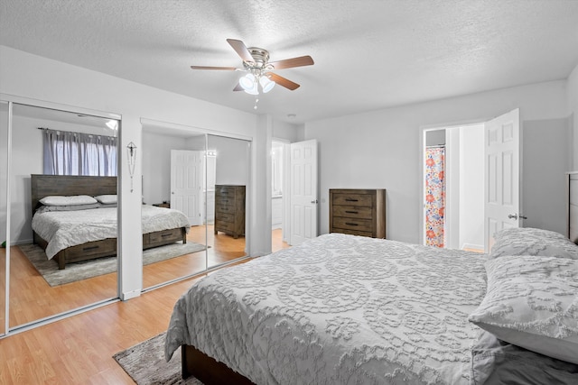 bedroom featuring a textured ceiling, ceiling fan, wood-type flooring, and two closets