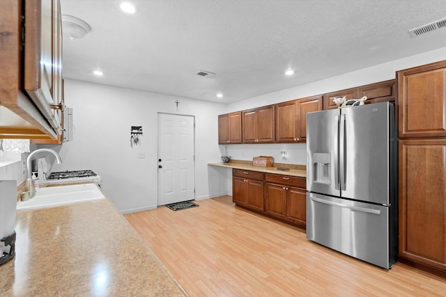 kitchen with stainless steel fridge, sink, a textured ceiling, and light wood-type flooring