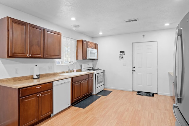 kitchen featuring a textured ceiling, sink, white appliances, and light wood-type flooring