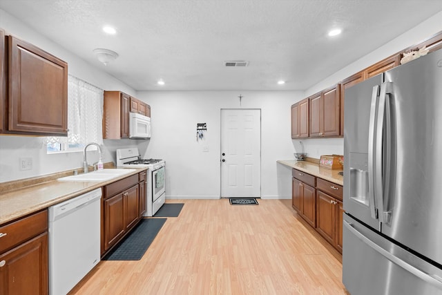 kitchen featuring a textured ceiling, sink, light hardwood / wood-style floors, and white appliances