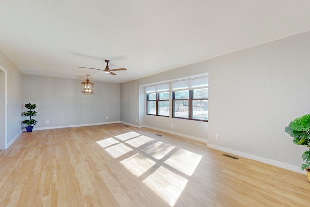 unfurnished room with ceiling fan with notable chandelier and light hardwood / wood-style flooring