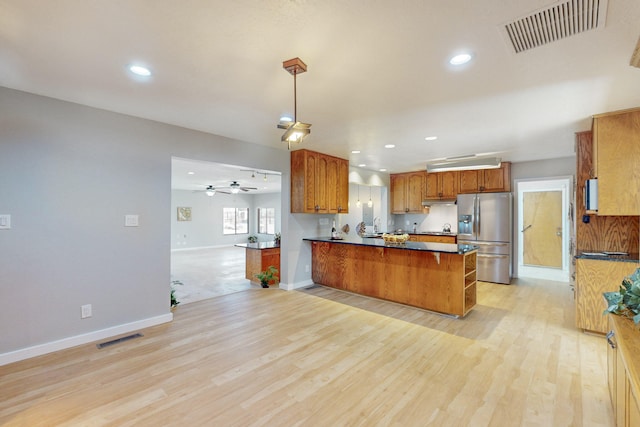 kitchen with kitchen peninsula, stainless steel refrigerator with ice dispenser, ceiling fan, light hardwood / wood-style floors, and hanging light fixtures