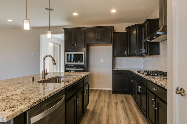 kitchen with wall chimney range hood, sink, light hardwood / wood-style flooring, appliances with stainless steel finishes, and decorative light fixtures