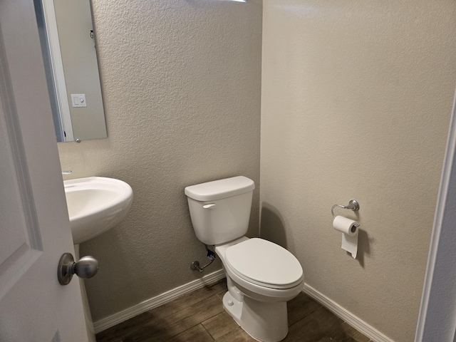 bathroom featuring toilet, baseboards, wood finished floors, and a textured wall