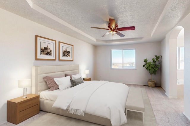 bedroom with a tray ceiling, ceiling fan, light carpet, and a textured ceiling