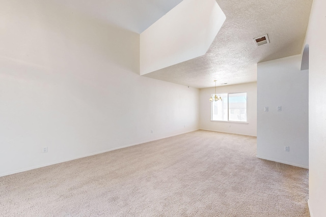 empty room with a textured ceiling, light colored carpet, and a notable chandelier