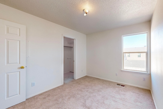 unfurnished bedroom with light colored carpet, a walk in closet, a textured ceiling, and a closet