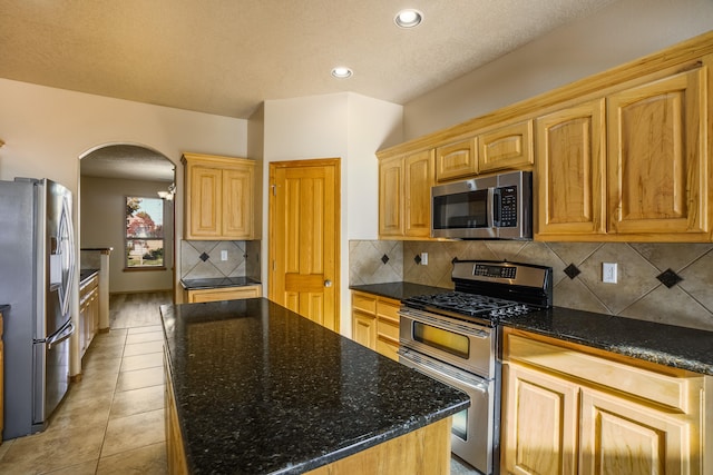 kitchen with a kitchen island, dark stone countertops, stainless steel appliances, and tasteful backsplash