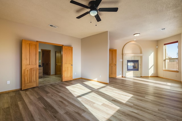 unfurnished living room with ceiling fan, a fireplace, wood-type flooring, and a textured ceiling