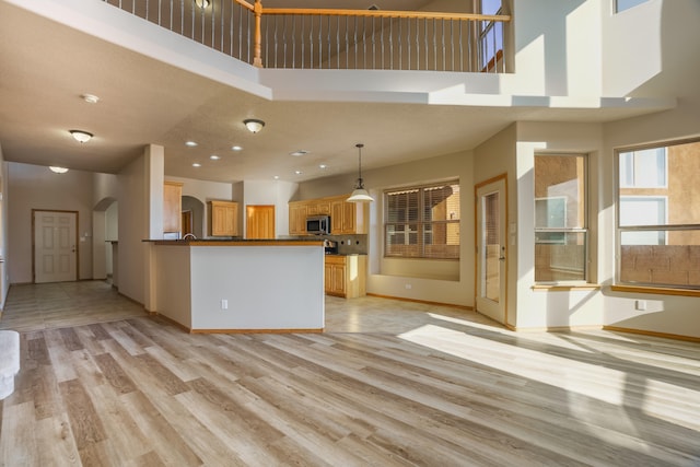 kitchen featuring pendant lighting, a towering ceiling, kitchen peninsula, and light hardwood / wood-style flooring