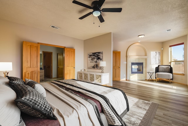 bedroom featuring ceiling fan, light hardwood / wood-style floors, a textured ceiling, and a tiled fireplace