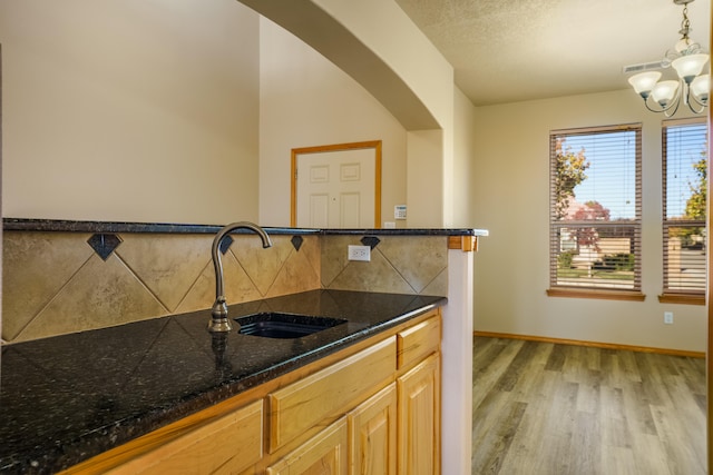 kitchen featuring tasteful backsplash, sink, light hardwood / wood-style flooring, a notable chandelier, and hanging light fixtures