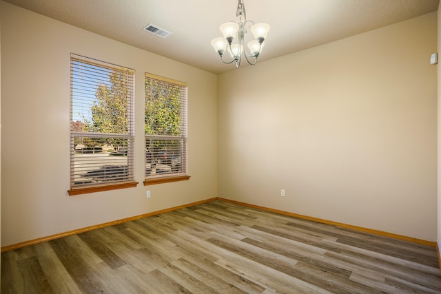 unfurnished room with light hardwood / wood-style floors, a textured ceiling, and an inviting chandelier