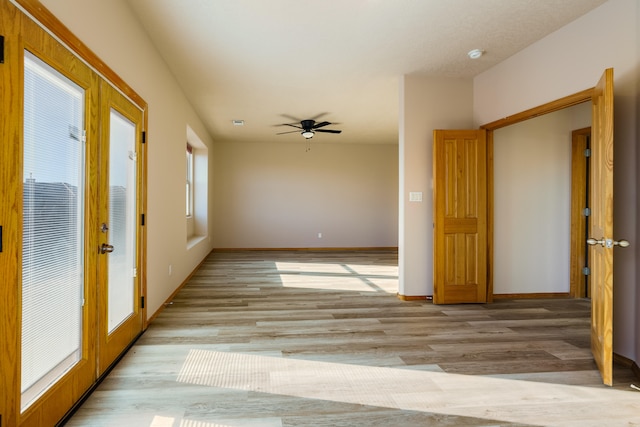 empty room featuring ceiling fan, french doors, and light wood-type flooring