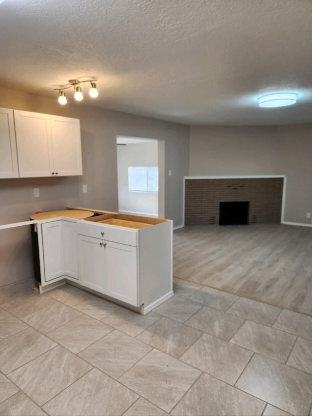 kitchen with white cabinetry, a textured ceiling, and a brick fireplace