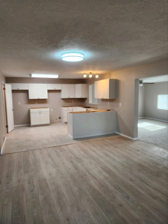 kitchen featuring light wood-type flooring, white cabinetry, and a textured ceiling