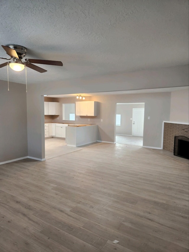 unfurnished living room featuring ceiling fan, light wood-type flooring, a textured ceiling, and a brick fireplace