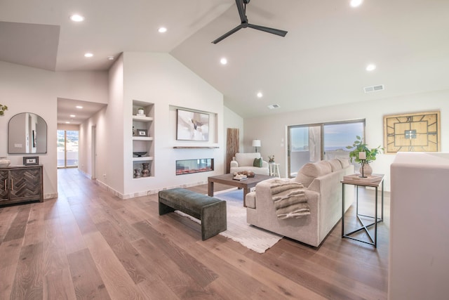 living room with built in shelves, light wood-type flooring, high vaulted ceiling, and ceiling fan