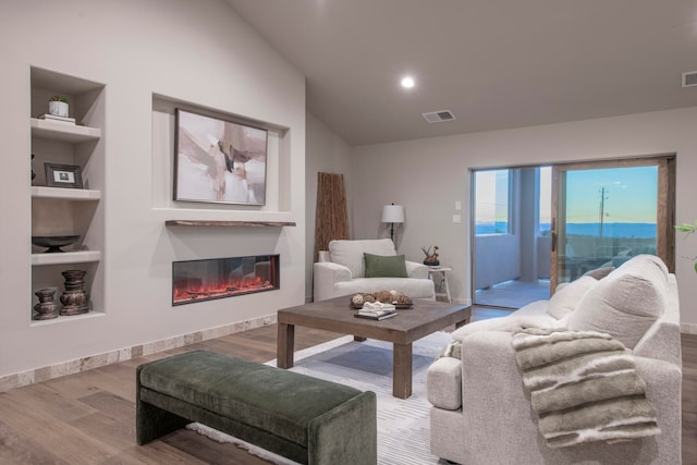 living room with built in features, hardwood / wood-style floors, and lofted ceiling