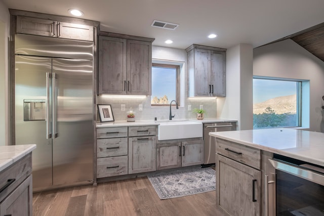 kitchen featuring sink, beverage cooler, tasteful backsplash, hardwood / wood-style floors, and appliances with stainless steel finishes