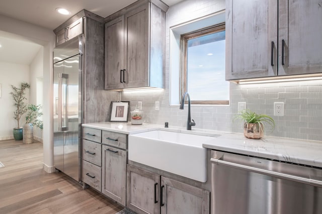 kitchen with sink, light wood-type flooring, appliances with stainless steel finishes, tasteful backsplash, and light stone counters