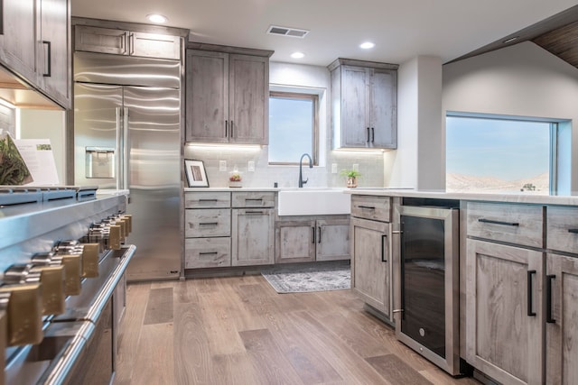 kitchen featuring tasteful backsplash, premium appliances, beverage cooler, sink, and light hardwood / wood-style flooring