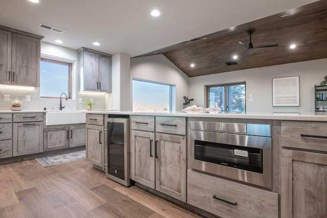 kitchen featuring sink, light hardwood / wood-style flooring, vaulted ceiling, tasteful backsplash, and beverage cooler