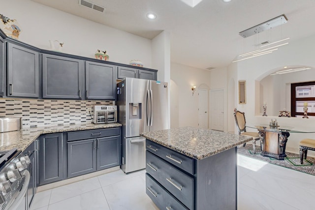 kitchen featuring a center island, tasteful backsplash, light tile patterned flooring, light stone counters, and stainless steel appliances