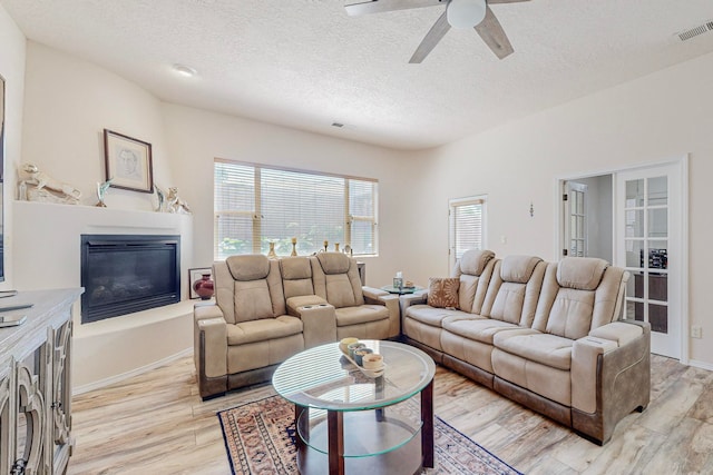 living room with ceiling fan, light hardwood / wood-style flooring, and a textured ceiling