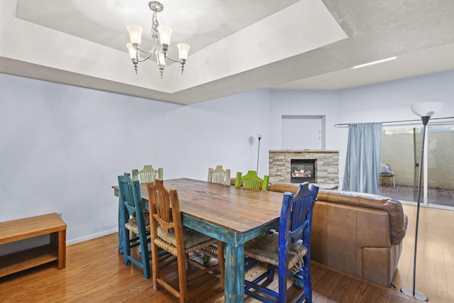 dining space featuring a raised ceiling, an inviting chandelier, hardwood / wood-style floors, and a stone fireplace